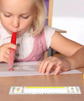 Child using colored marker at desk with clear adhesive pocket holding alphabet nameplate