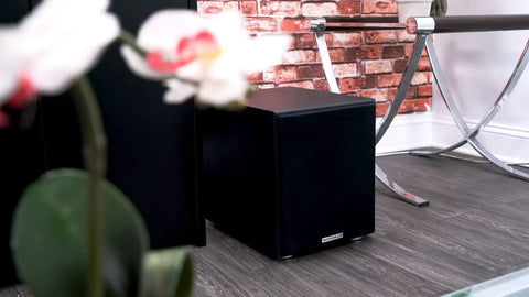 Shaker 8 Inch Powered Subwoofer With 400W Peak 200W RMS Class D Amplifier in a modern living room setting next to furniture.