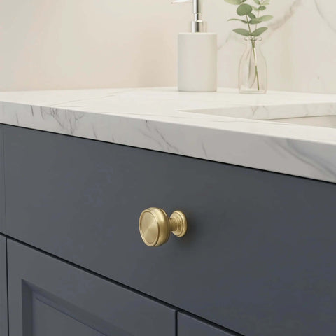 Brushed gold knob on navy kitchen cabinet drawer with marble countertop