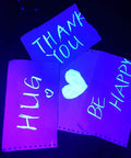 Fluorescent posters under 8W UV LED black light with glowing neon words: Thank You, Hug, Be Happy, & Heart symbol.