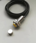 Front view of M18 proximity sensor with yellow actuator, threaded metal body, and attached cable; separate magnet shown.