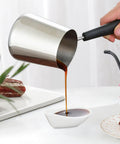 Person pouring coffee from Turkish Coffee Pot And Milk Frothing Jug 21oz 600ml Stainless Steel Toroid Pitcher with long handle.