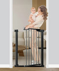 Woman holding child by narrow baby gate for doorways and stairs 24.5 to 28.3 inch wide pressure mounted walk through child safety gate black.