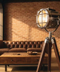 Nautical Style Chrome Spotlight Floor Lamp With Brown Wood Tripod Stand in a vintage brick-walled living room setting