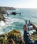 Person flying Air 3S Drone With RC 2 Fly More Bundle For Travel And Content Creation over rocky coastline, using remote control.