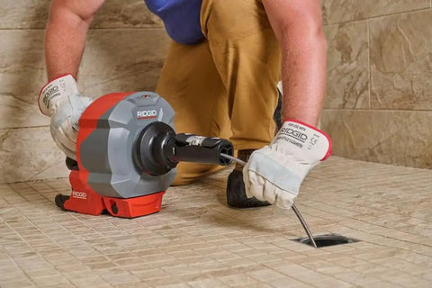 Heavy Duty Cordless Drain Snake With Brushless Motor And Twenty Five Foot Steel Cable Blasts Away Stubborn Clogs being used on a shower drain.