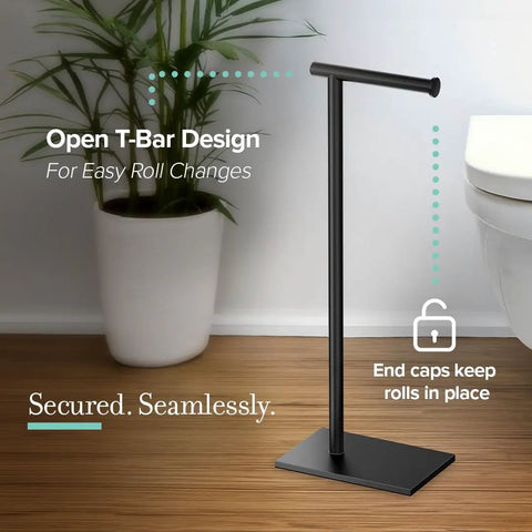 Modern Square Base Toilet Paper Holder Stand In Matte Black No Drill Install Free Weighted And Padded Base For Stable Rust Resistant Metal Bathroom Accessory 22.25 Inch Tall shown on bathroom floor with plant in background.