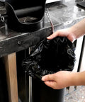 Person holding espresso knock box garbage bag, 13x35 inches, for floor standing bins, heavy duty, eco-friendly, commercial use.