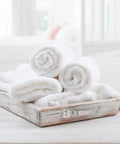 Four rolled white towels in a rustic wooden tray on a bathroom counter.