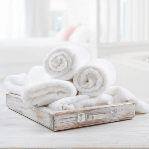 Four rolled white towels in a rustic wooden tray on a bathroom counter.