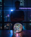 LED Skull Table Lamp With Gothic Glow Battery Powered Three AAA Batteries Needed, lit on desk with city backdrop at night, 15 cm tall