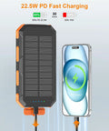 Portable Solar Power Bank 38800mAh With PD 22.5W USB C Fast Charging Four Built In Cables Dual LED Emergency Flashlights shown charging phone
