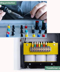Close-up of hands soldering with welding tools and a yellow transformer unit with wires in an industrial setting.