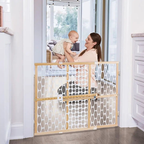 Mother holding baby over Wooden Baby Gate With Mesh For Doorways, Quick Fit Pressure Mounted, Adjustable 26.5 to 42 Inches Wide, 23 Inches Tall