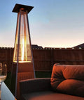 Outdoor scene with a lit 4-sided glass tube patio heater and seating area at sunset. Heat Reflector Shield For Glass Tube Heater 4 Sided Pyramid Patio Heater Replacement Top Easy Install Eighteen And A Half Inches Square With Three Pre Drilled Holes Spaced Two And Three Quarters Inches Fits Most 4 Sided Glass Tube Patio Heaters.