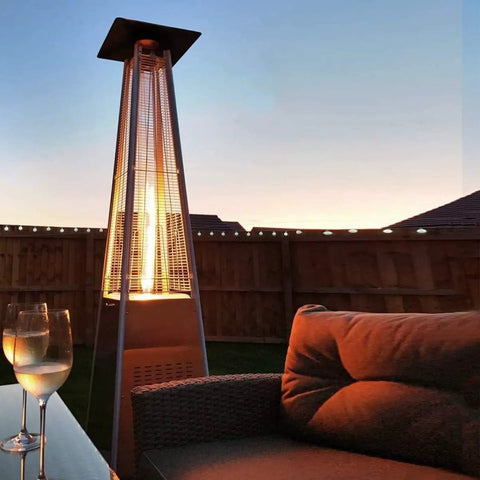 Outdoor scene with a lit 4-sided glass tube patio heater and seating area at sunset. Heat Reflector Shield For Glass Tube Heater 4 Sided Pyramid Patio Heater Replacement Top Easy Install Eighteen And A Half Inches Square With Three Pre Drilled Holes Spaced Two And Three Quarters Inches Fits Most 4 Sided Glass Tube Patio Heaters.