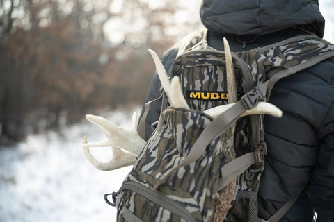 Hunter wearing Pro 1075 Backpack in Mossy Oak Bottomland Camo with antlers, wide padded shoulders, ideal for quiet hunting.