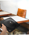 Built Tough Cast Iron Table Leg Brackets With Five Hole Mounting Plates displayed in hand against a wooden table backdrop.