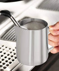 Person holding Milk Frothing Pitcher 12oz And 20oz Stainless Steel Jug For Espresso Machines And Latte Art, steaming milk