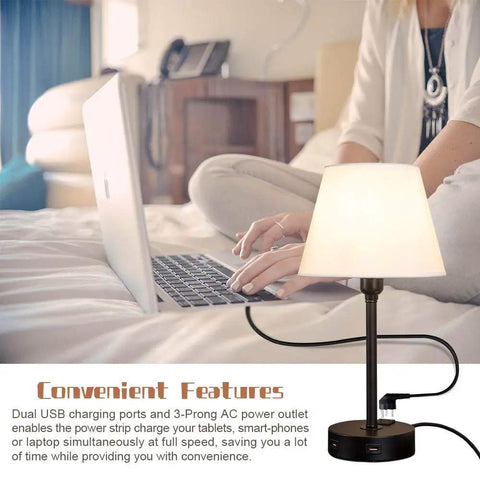 Lit Touch Control Table Lamp With Dual USB Ports And AC Outlet, showing warm light next to a person using a laptop in a bedroom.