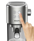 Close-up of a hand pressing buttons on a KRUPS semi automatic espresso coffee maker with built in steam wand.
