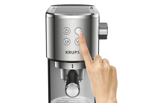Close-up of a hand pressing buttons on a KRUPS semi automatic espresso coffee maker with built in steam wand.