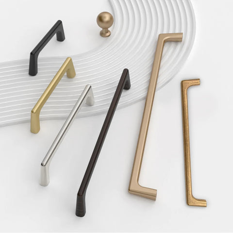 Various cabinet handles in different finishes, including brushed satin nickel, arranged on a textured surface.
