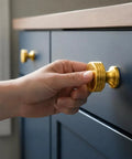 Slick Brushed Gold Cabinet Knobs Two Pack Modern Three Groove Handle Style with hand grasping knob on dark drawer.