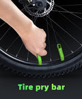 Two green tire levers (tire pry bars) for MTB tires being used to pry a bead from a 29-inch wheel with a disc rotor.