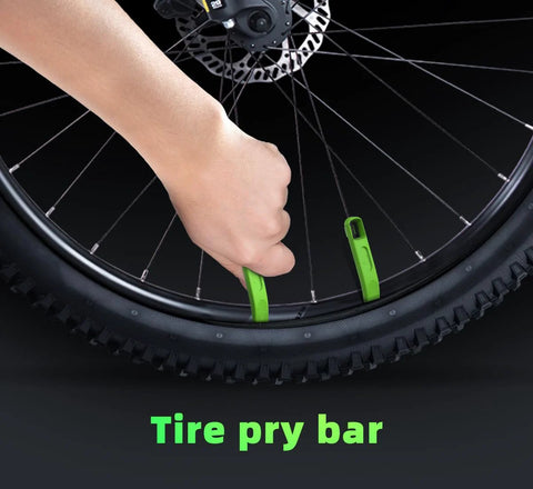 Two green tire levers (tire pry bars) for MTB tires being used to pry a bead from a 29-inch wheel with a disc rotor.