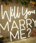 Will You Marry Me Neon Sign LED Proposal Light With Acrylic Backboard Large Marry Me Decor placed on wire backdrop with pink flowers