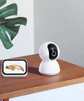 360 Degree All-In-One Home Security Cam 2K With AI Human Detection on wooden table next to digital pet monitor.