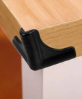 Black silicone corner guard on wooden table edge, part of Silicone Corner Guards 4 Pack For Furniture And Tables, Easy To Install Edge Bumpers