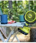 Cordless 4 Inch Clamp Fan Kit With 18V Ryobi Battery, Charger, And Pocket Flashlight on a table in an outdoor setting