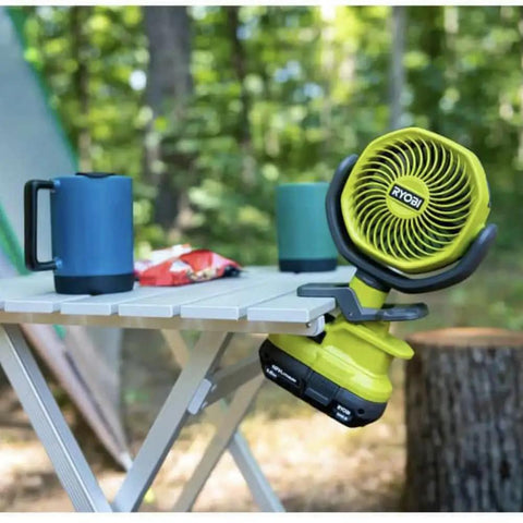Cordless 4 Inch Clamp Fan Kit With 18V Ryobi Battery, Charger, And Pocket Flashlight on a table in an outdoor setting