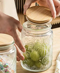 Hands lifting bamboo lid of Vintage Glass Jar With Lid 23.7oz Airtight Food Storage for Coffee, Tea, Sugar and Snacks.