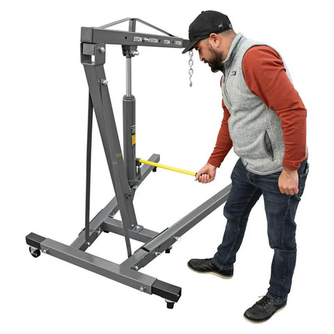 Heavy Duty Folding Shop Crane With Hydraulic Engine Hoist Six Wheel Base And Safety Brakes Badass Steel Frame For Auto Mechanics shown in use.