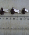 Six Black Universal Zipper Repair Kit Sliders Instant Fix for Jackets Bags and Pants near ruler for size reference.