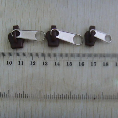 Six Black Universal Zipper Repair Kit Sliders Instant Fix for Jackets Bags and Pants near ruler for size reference.