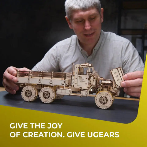 Cargo Truck 3D Puzzle Kit For Adults With Spring Powered Mechanics, Realistic Wooden Model Truck Build Featuring Three Axles And Differentials, Brain Teaser Hobby Set For Makers And Auto Enthusiasts. Man assembling wooden cargo truck model
