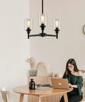 Industrial Glass Cylinder Pendant Chandelier in Black, 6 Light Farmhouse Vibe for Dining Room, shown above a wooden table