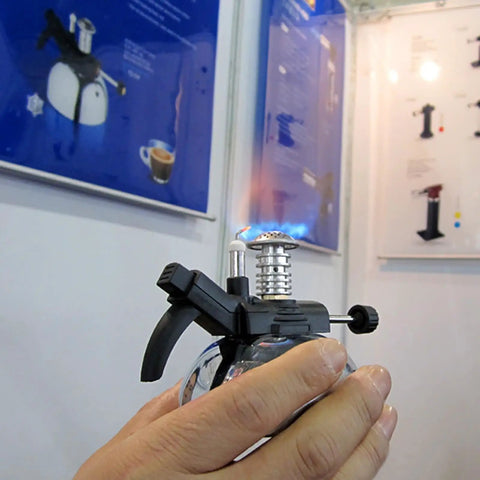 Person holding Ultra Portable Mini Butane Burner For Coffee Or Lab Use, Lightweight Bunsen Style Gas Stove with visible flame