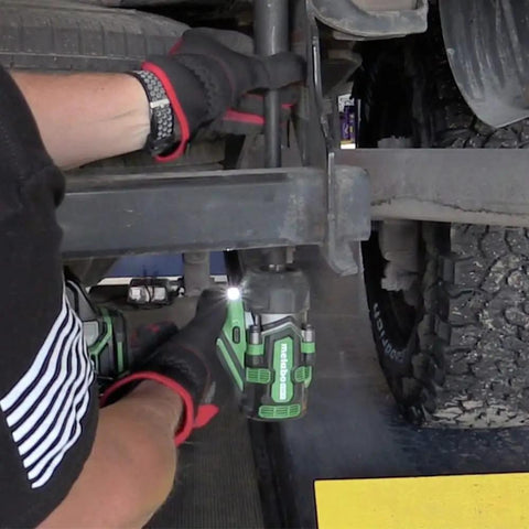 Mechanic using 36V MultiVolt Half Inch Mid Torque Cordless Impact Wrench Workhorse Tool with LED Light under a vehicle