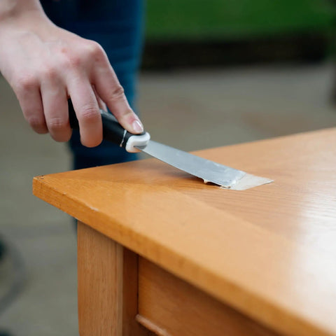 Applying Plastic Wood All Purpose Latex Wood Filler Natural 3 Oz for quick wood repair on furniture surface with putty knife.