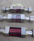 Three stainless steel waterjet intensifier assemblies with red cores and silver end caps on concrete