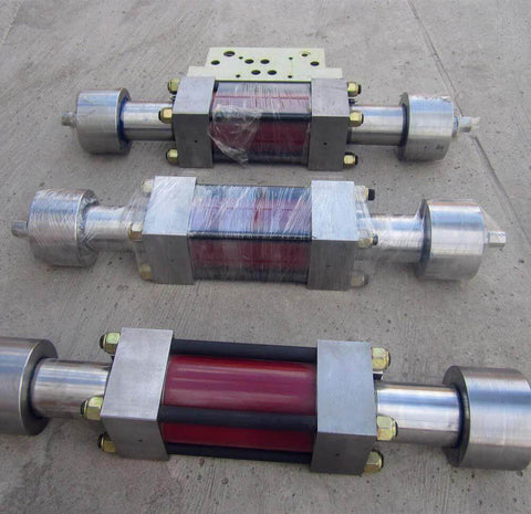 Three stainless steel waterjet intensifier assemblies with red cores and silver end caps on concrete