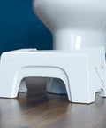Fold N Stow Compact Foldable Toilet Stool White 8 Inch Space Saving Design beside toilet on wooden floor
