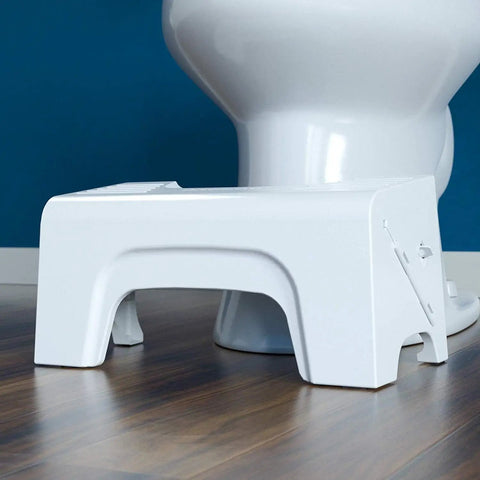 Fold N Stow Compact Foldable Toilet Stool White 8 Inch Space Saving Design beside toilet on wooden floor