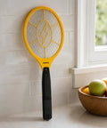 Powerful Handheld Bug Zapper For Home And Outdoors leaning against a tiled wall, showing electric mosquito killer racket with yellow frame and 3-layer grid.