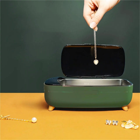 Hand placing heart necklace into Compact 40khz Ultrasonic Cleaner For Jewelry And Personal Care Devices on orange surface.